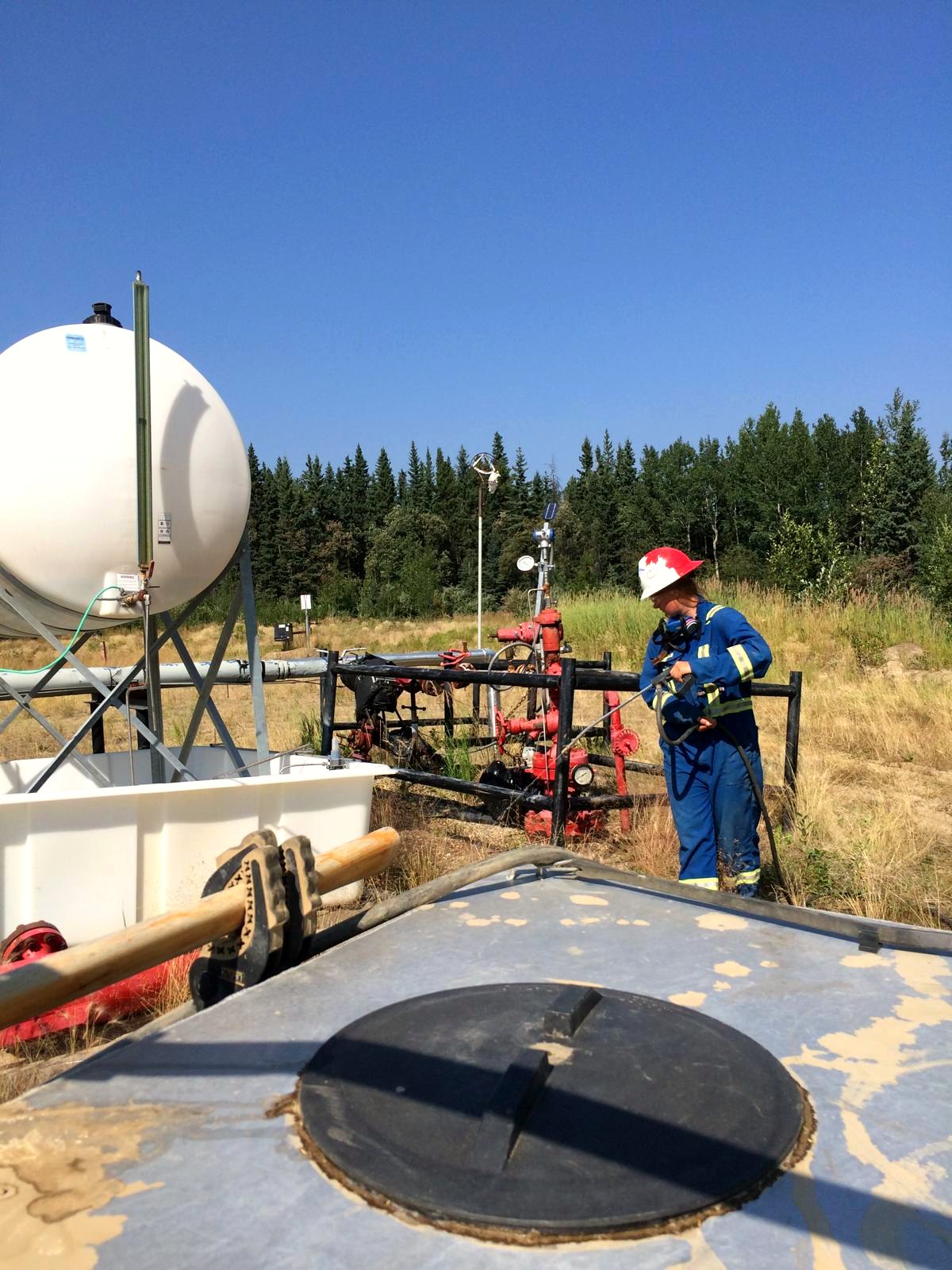 Certified applicator spraying vegetation at a wellsite tank battery