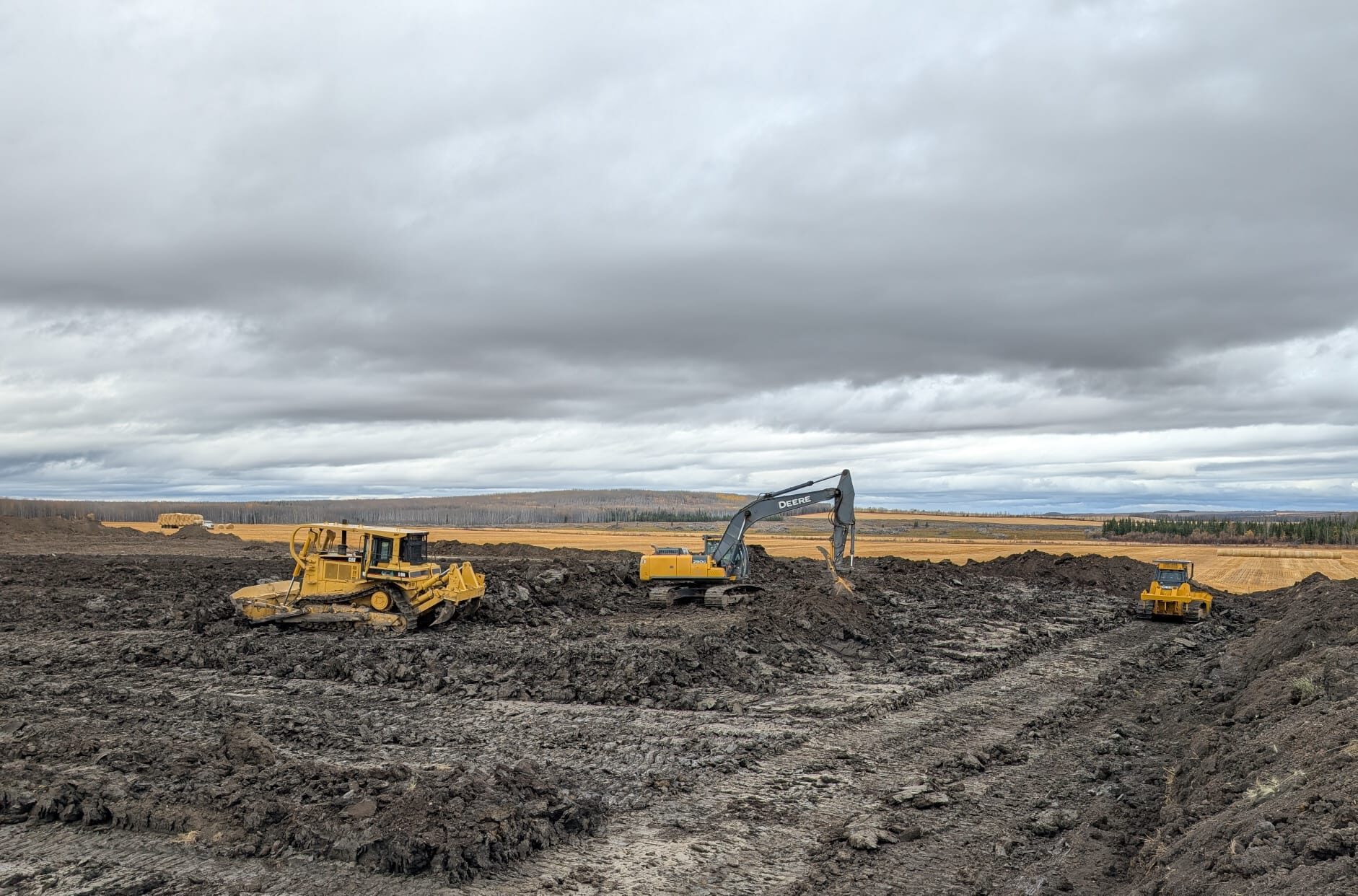 Dozer, excavator and packer working on an industrial wellsite project near Fort St. John