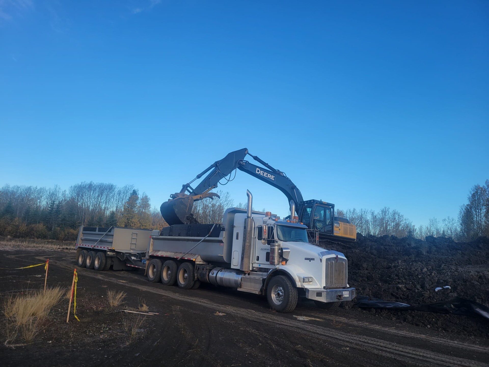 Excavator loading soil into a truck and trailer on an industrial remediation project