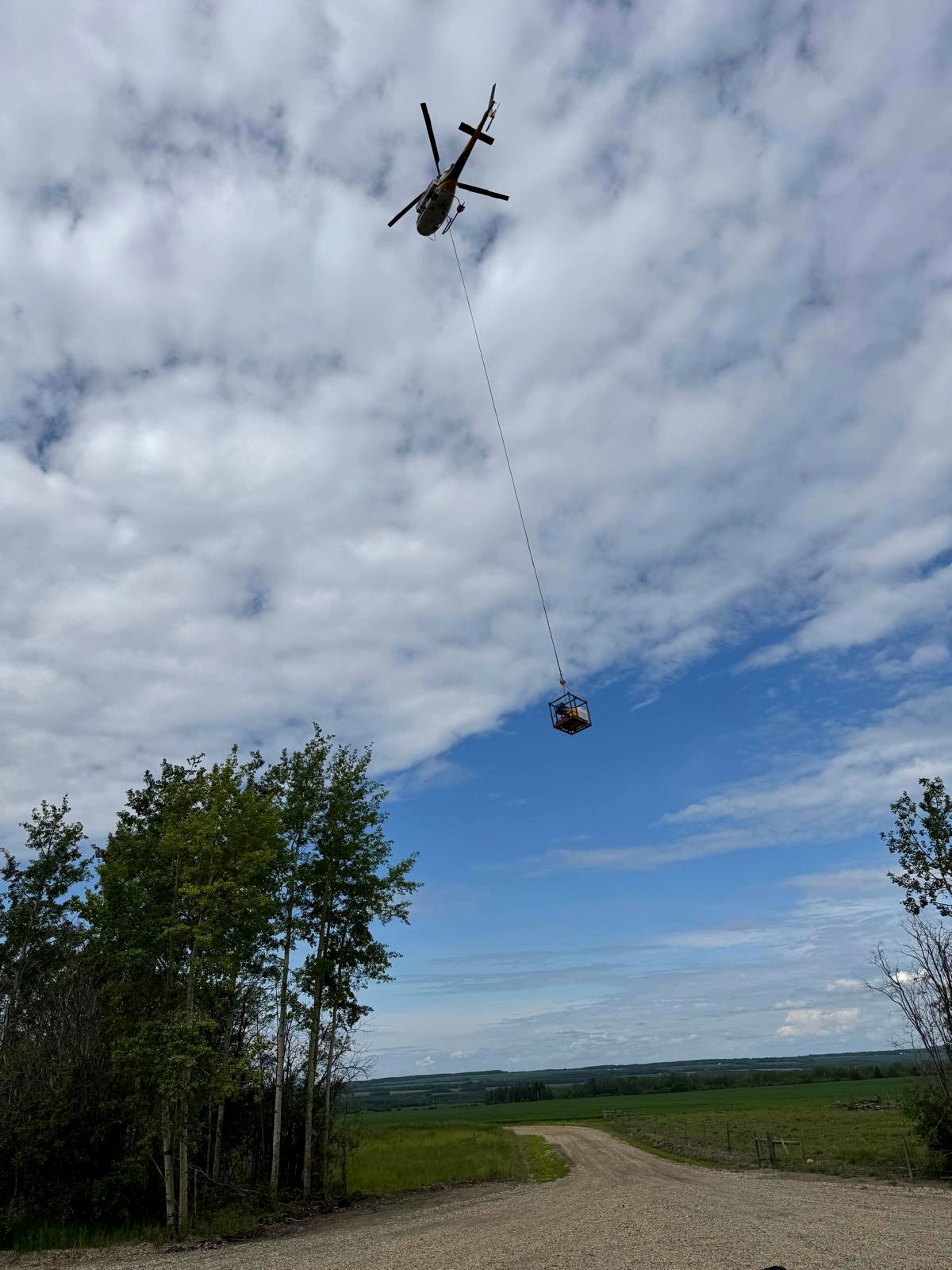 Helicopter lifting a personnel basket on a longline into a remote weed control site in Northeast BC