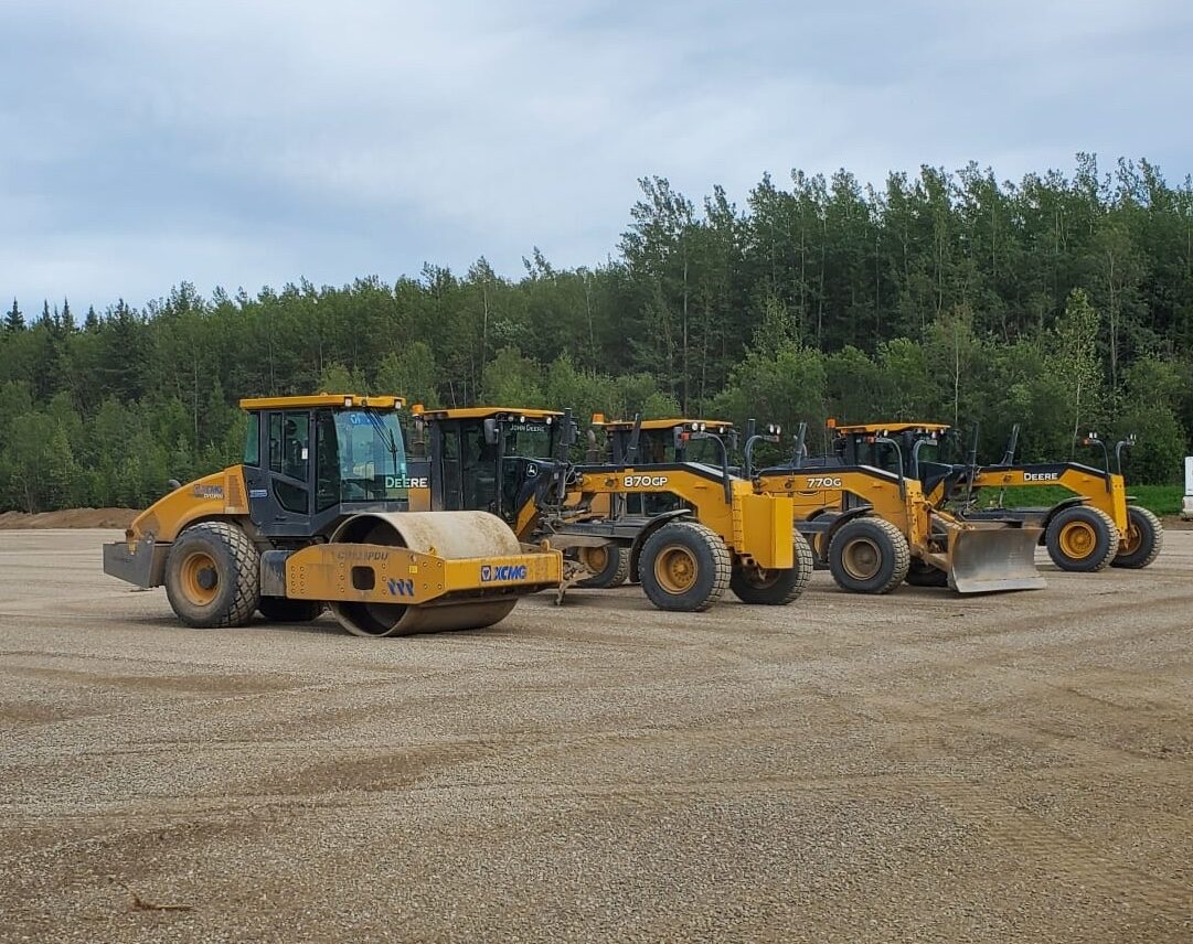 Compaction roller and motor graders lined up on a gravel pad near Fort St. John