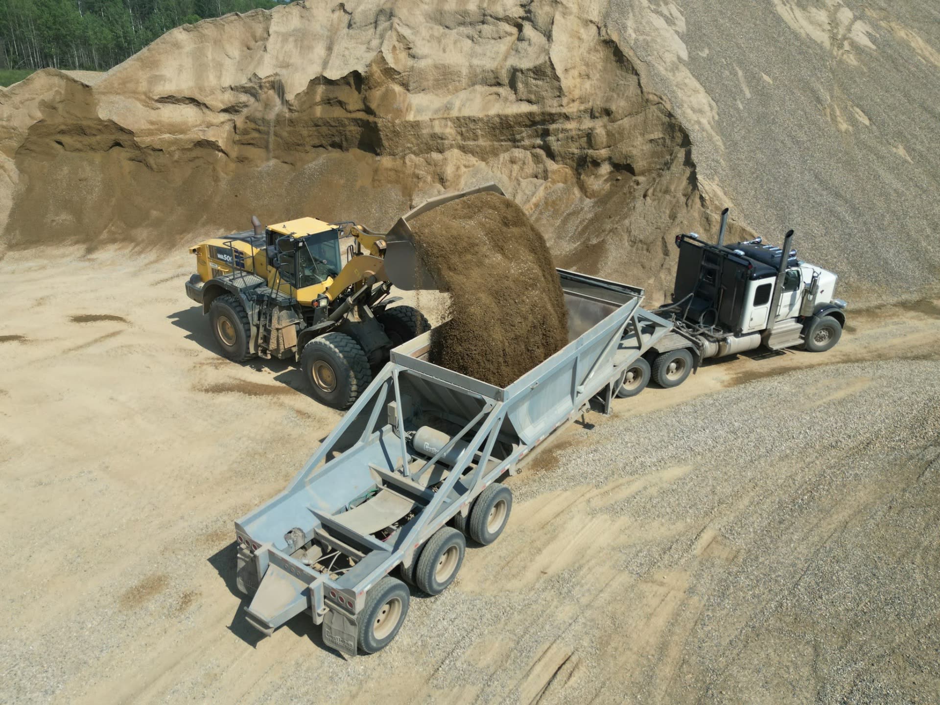 Loader placing crushed gravel into a highway truck and trailer for delivery