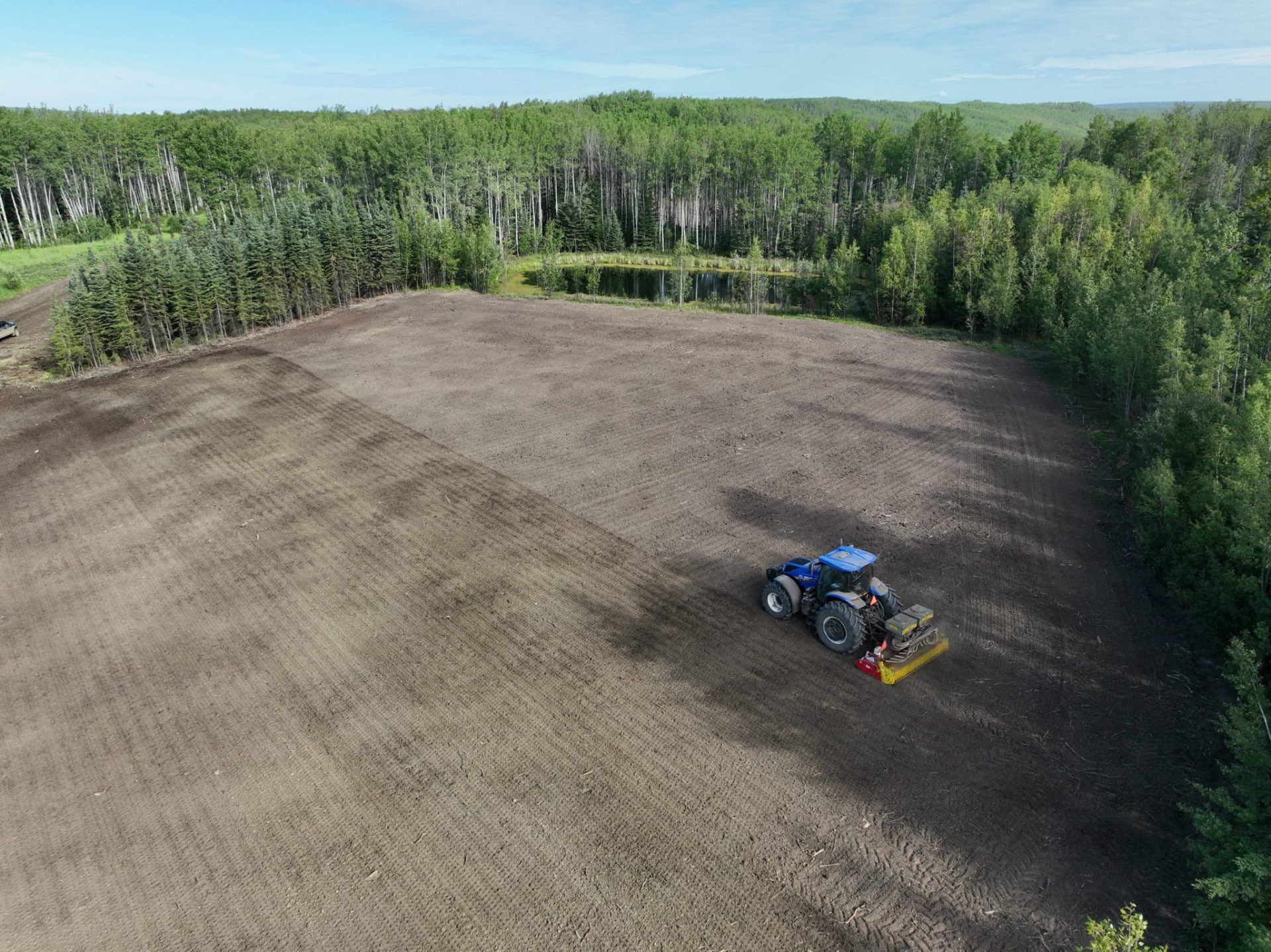 Tractor seeding a recontoured wellsite during reclamation work in Northeast BC