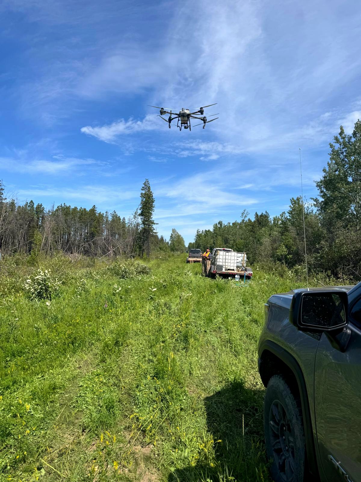 Spray drone operating over a right-of-way with a support truck and water tanks